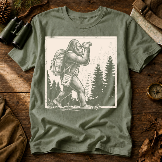 Bigfoot Birdwatching Field Guide Tee in Bay, centered front design on a birdwatching flat-lay mockup