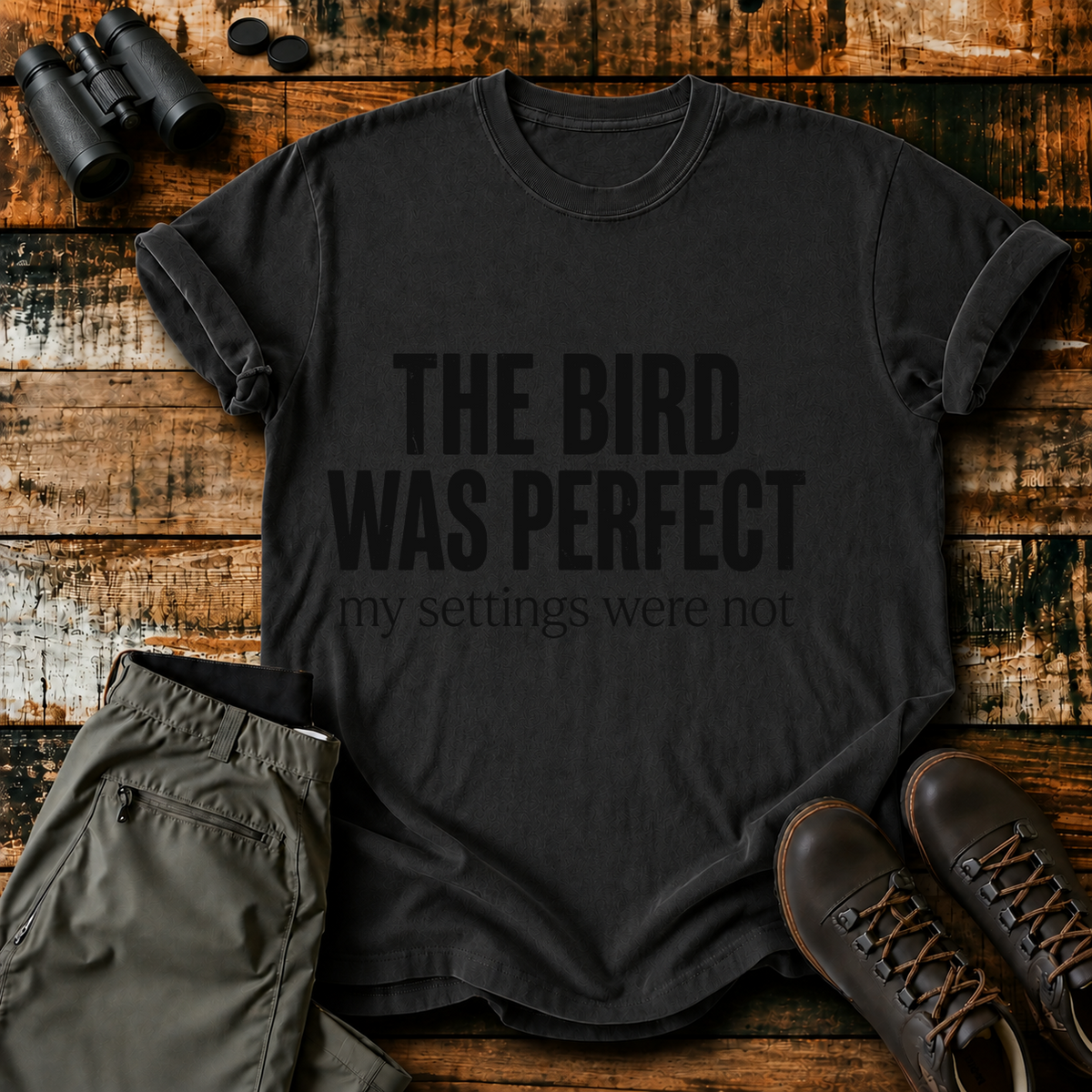 The Bird Was Perfect My Settings Were Not Tee in Black, centered front design on a birdwatching flat-lay mockup