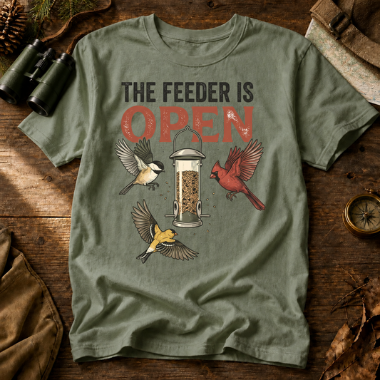 The Feeder Is Open Backyard Birds Tee in Bay, centered front design on a birdwatching flat-lay mockup