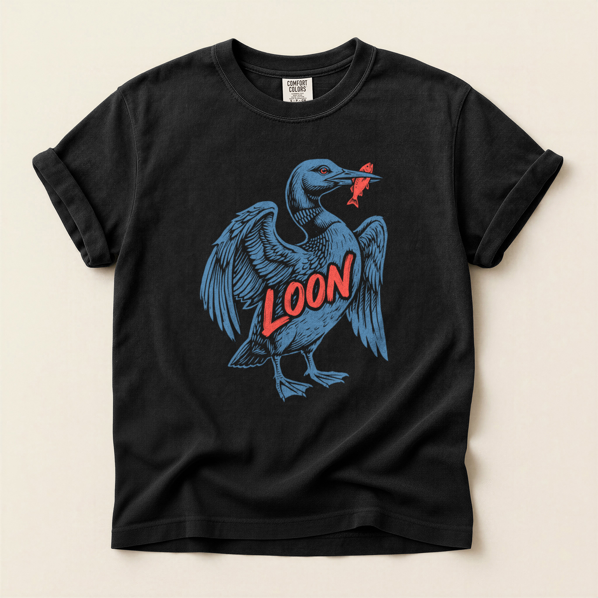 Loon Catches Fish T-Shirt in Bay laid beside field gear