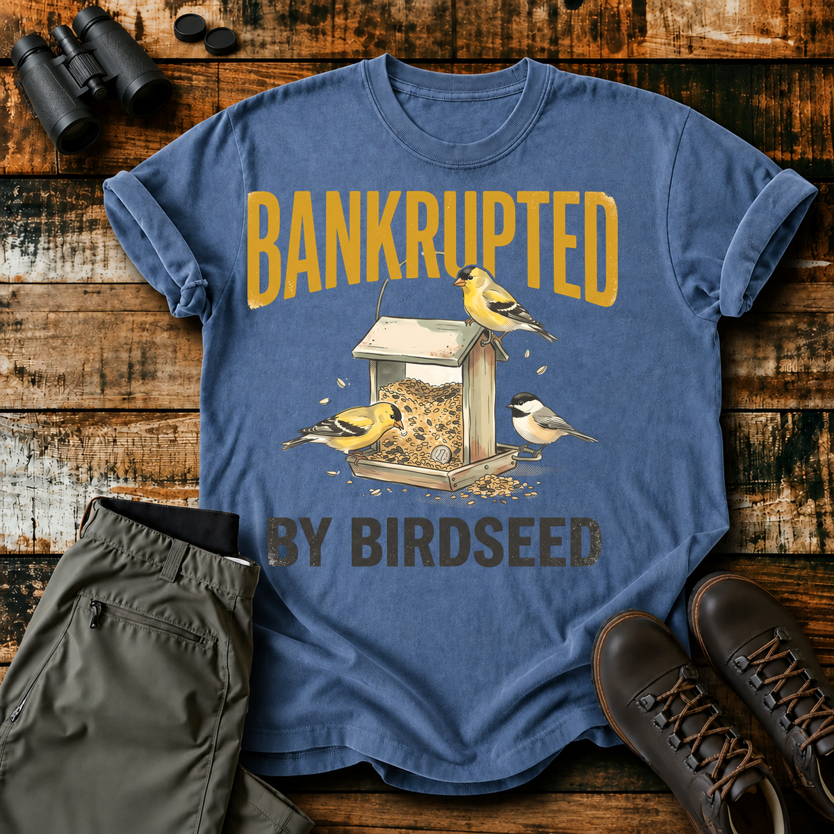 Bankrupted by Birdseed Backyard Birds Tee in Blue Jean, centered front design on a birdwatching flat-lay mockup
