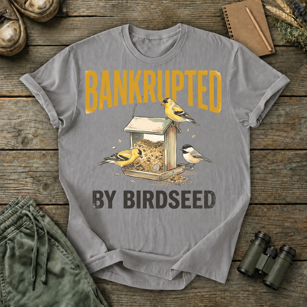 Bankrupted by Birdseed Backyard Birds Tee in Grey, centered front design on a birdwatching flat-lay mockup