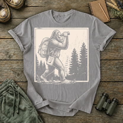 Bigfoot Birdwatching Field Guide Tee in Grey, centered front design on a birdwatching flat-lay mockup