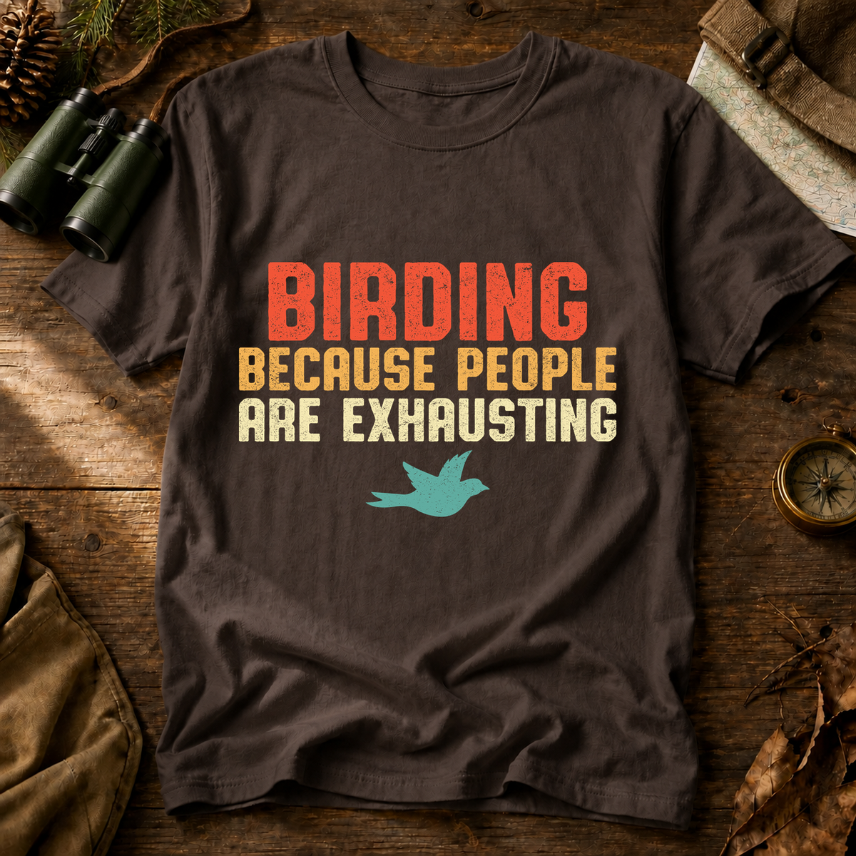 Birding Because People Are Exhausting Tee in Espresso, centered front design on a birdwatching flat-lay mockup