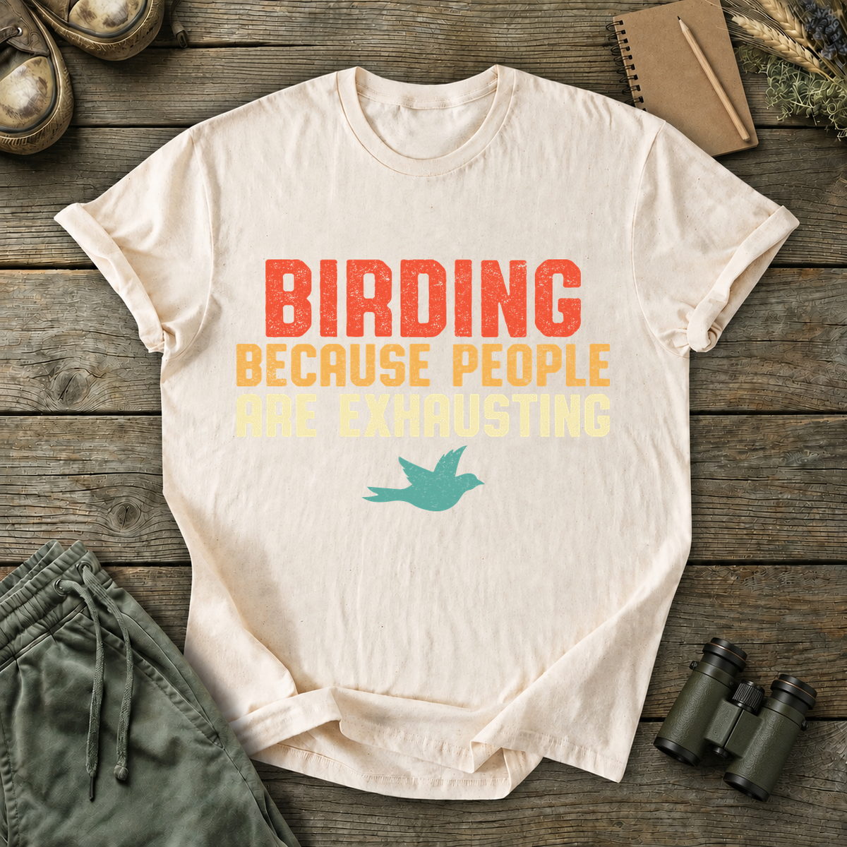Birding Because People Are Exhausting Tee in Ivory, centered front design on a birdwatching flat-lay mockup
