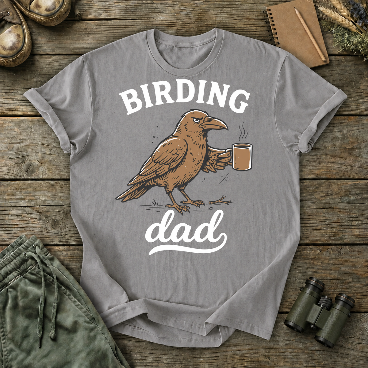 Birding Dad Coffee Bird Tee in Grey, centered front design on a birdwatching flat-lay mockup