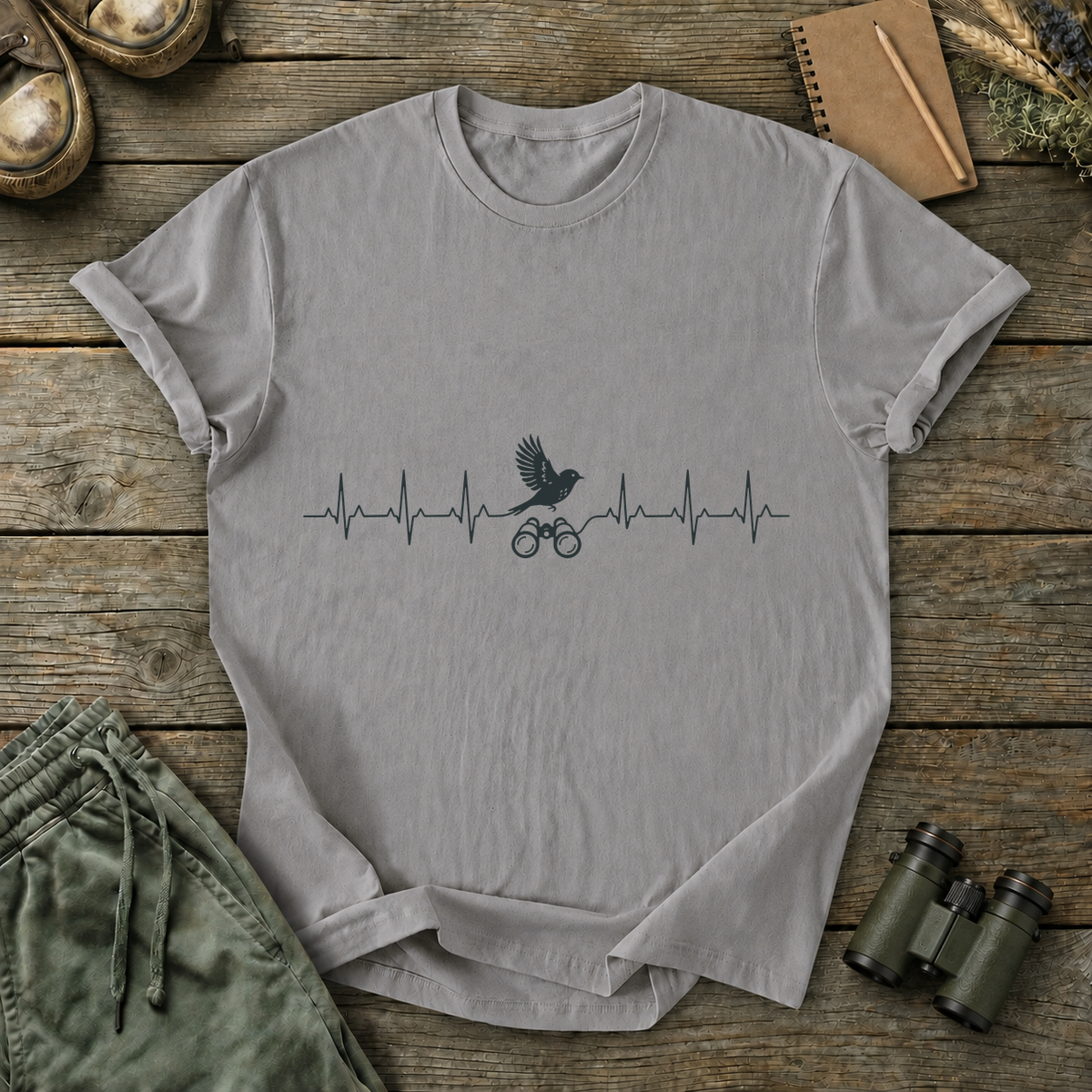 Birding Heartbeat Tee in Grey, centered front design on a birdwatching flat-lay mockup