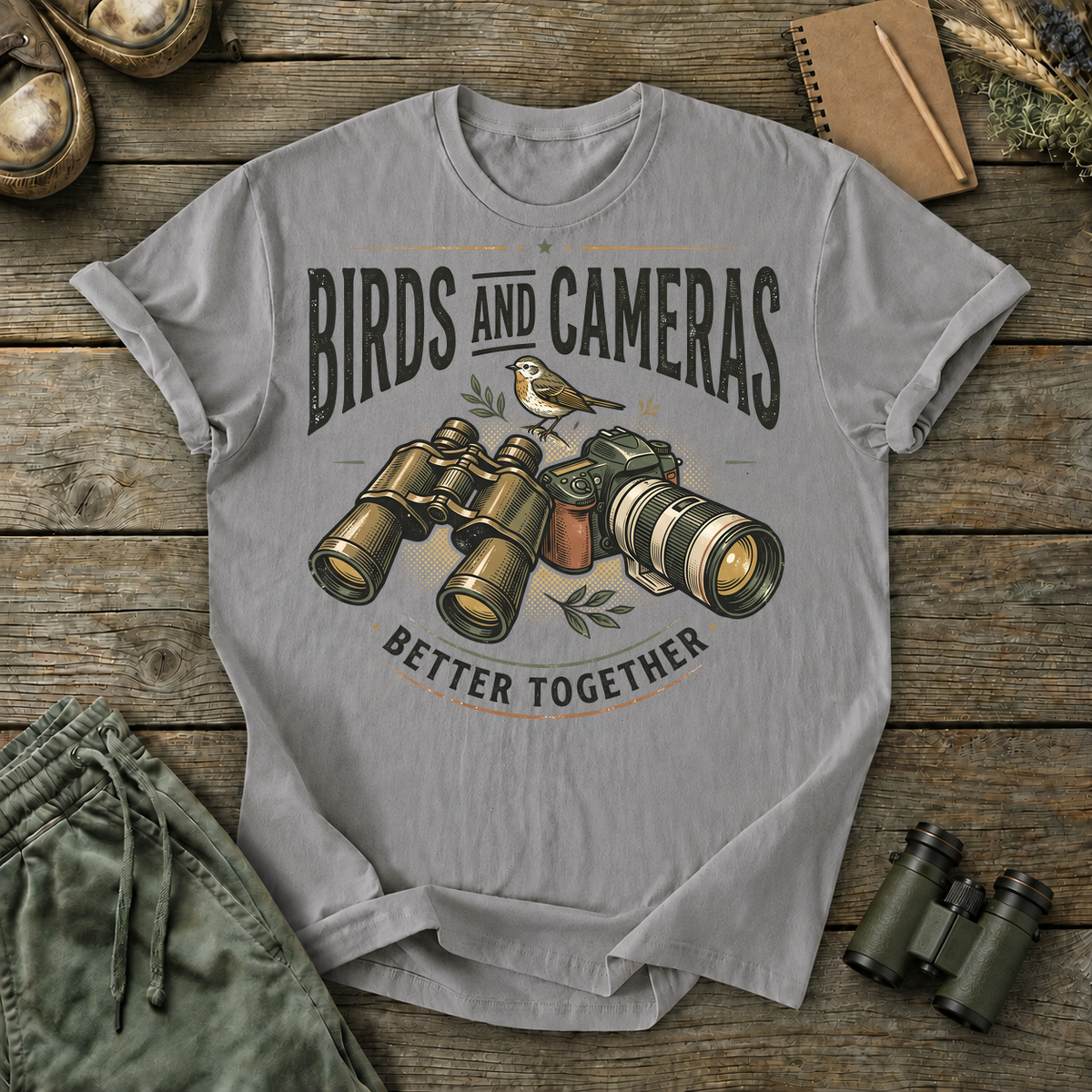 Birds and Cameras Better Together Tee in Grey, centered front design on a birdwatching flat-lay mockup