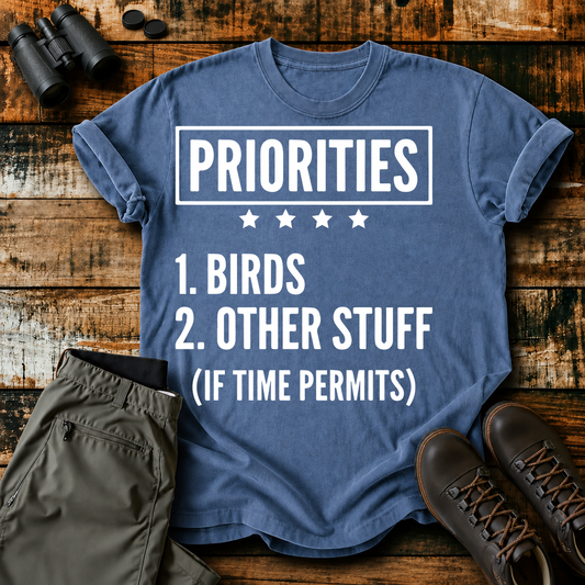 Birds First Priorities Tee in Blue Jean, centered front design on a birdwatching flat-lay mockup
