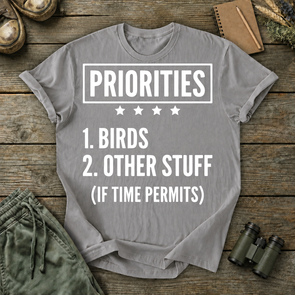 Birds First Priorities Tee in Grey, centered front design on a birdwatching flat-lay mockup