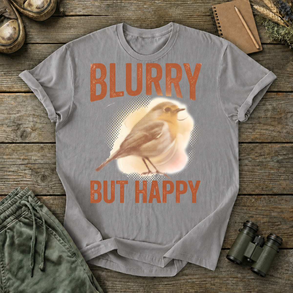Blurry but Happy Bird Photography Tee in Grey, centered front design on a birdwatching flat-lay mockup