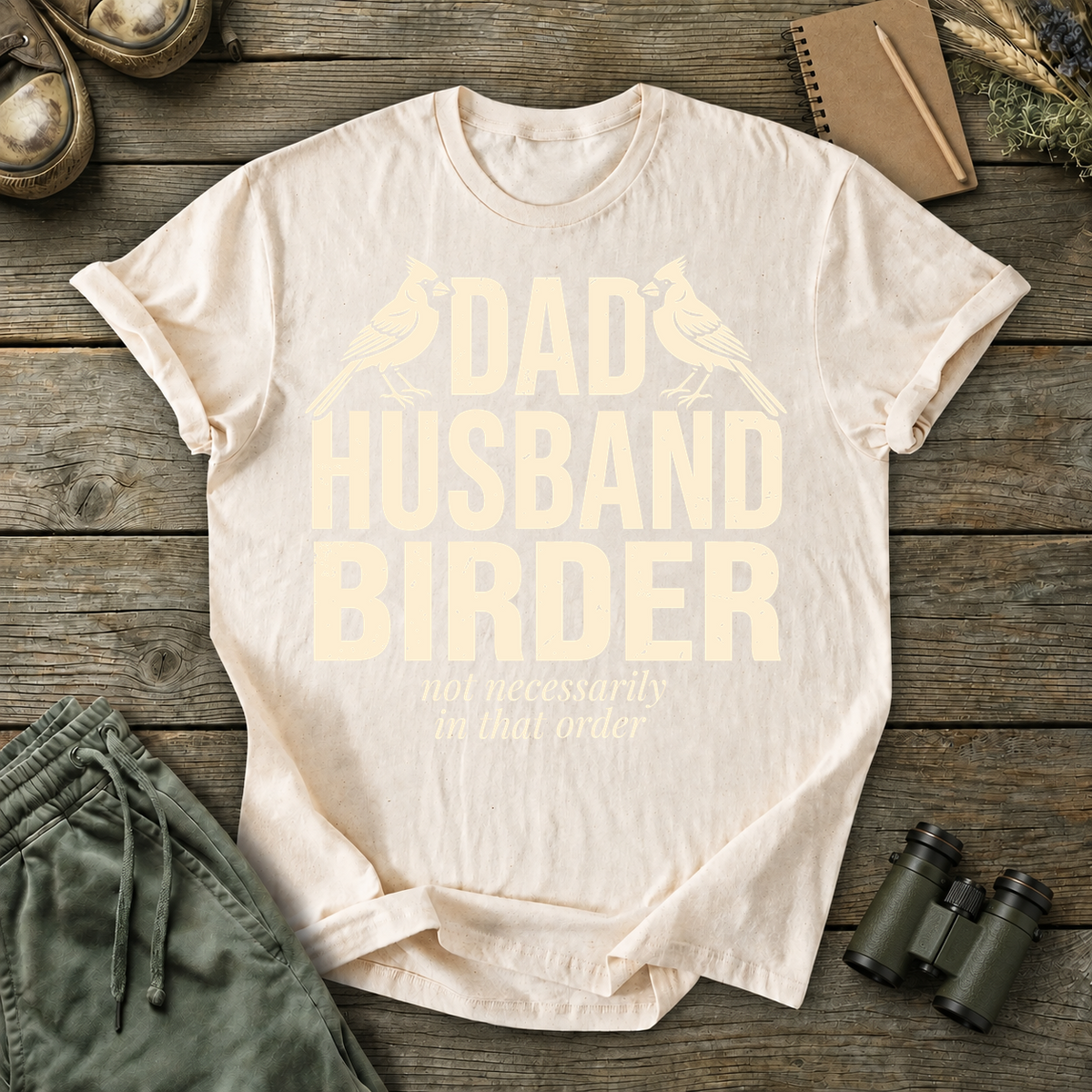 Dad Husband Birder Tee in Ivory, centered front design on a birdwatching flat-lay mockup