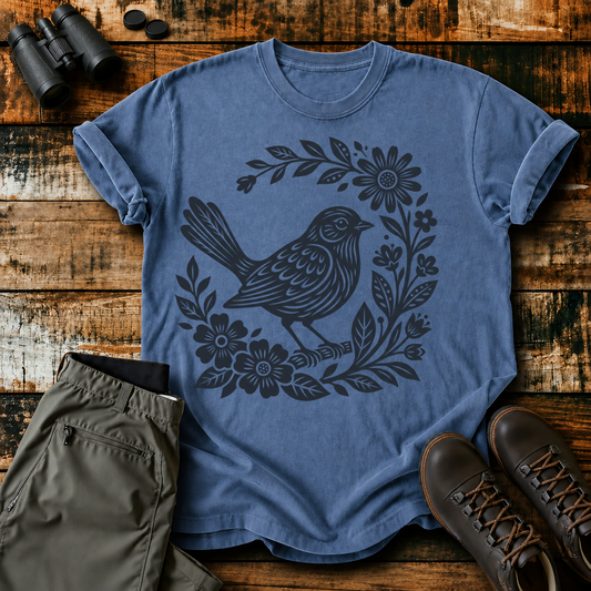 Folk Floral Songbird Tee in Blue Jean, centered front design on a birdwatching flat-lay mockup