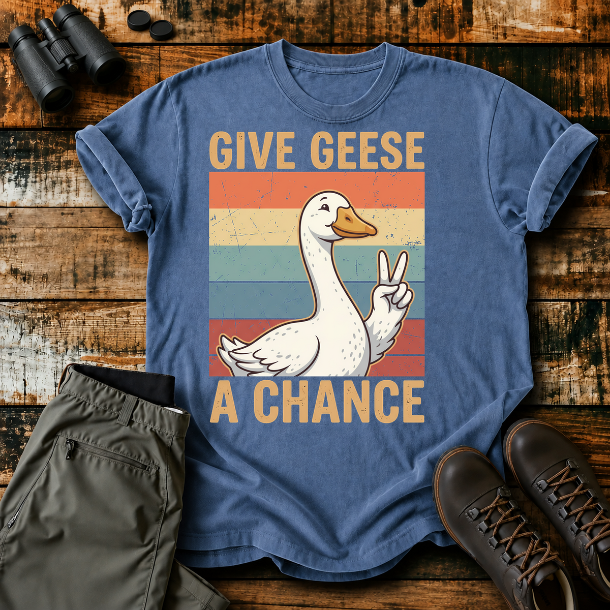 Give Geese a Chance Tee in Blue Jean, centered front design on a birdwatching flat-lay mockup