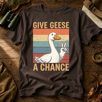 Give Geese a Chance Tee in Espresso, centered front design on a birdwatching flat-lay mockup