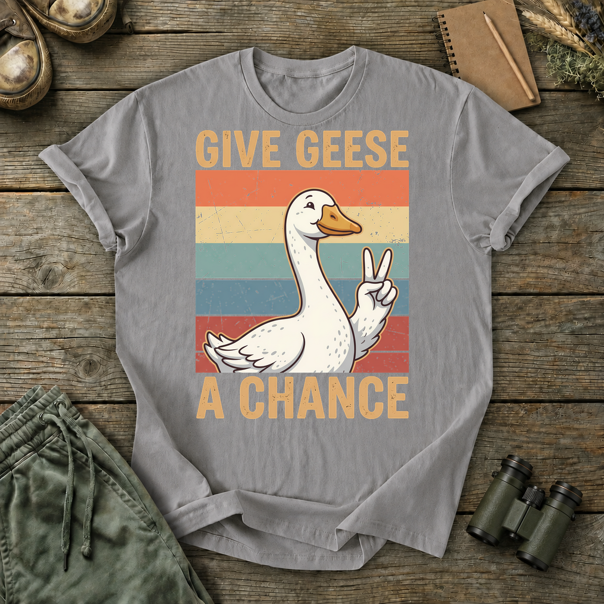 Give Geese a Chance Tee in Grey, centered front design on a birdwatching flat-lay mockup