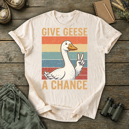 Give Geese a Chance Tee in Ivory, centered front design on a birdwatching flat-lay mockup
