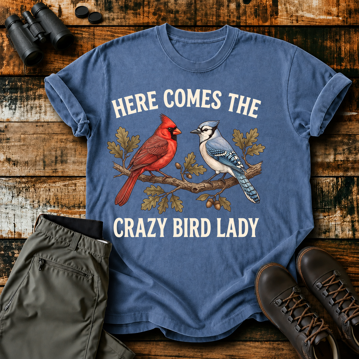 Here Comes the Crazy Bird Lady Tee in Blue Jean, centered front design on a birdwatching flat-lay mockup