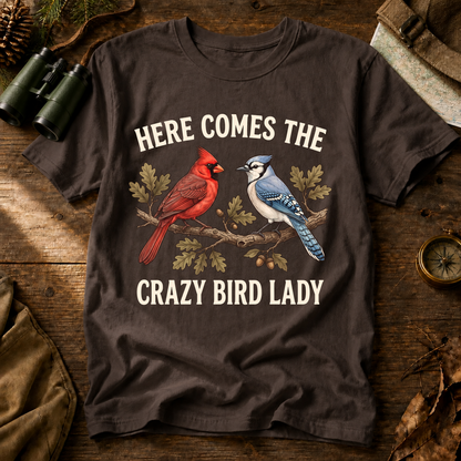 Here Comes the Crazy Bird Lady Tee in Espresso, centered front design on a birdwatching flat-lay mockup