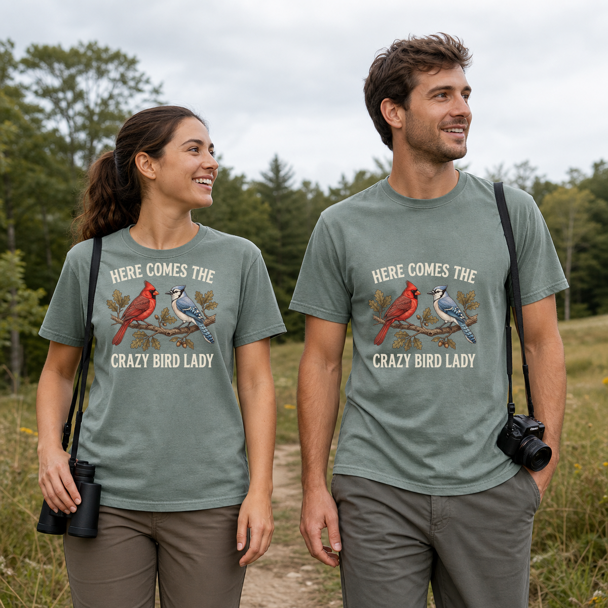 Female and male models wearing the Here Comes the Crazy Bird Lady Tee in Bay, with the artwork centered on both shirts