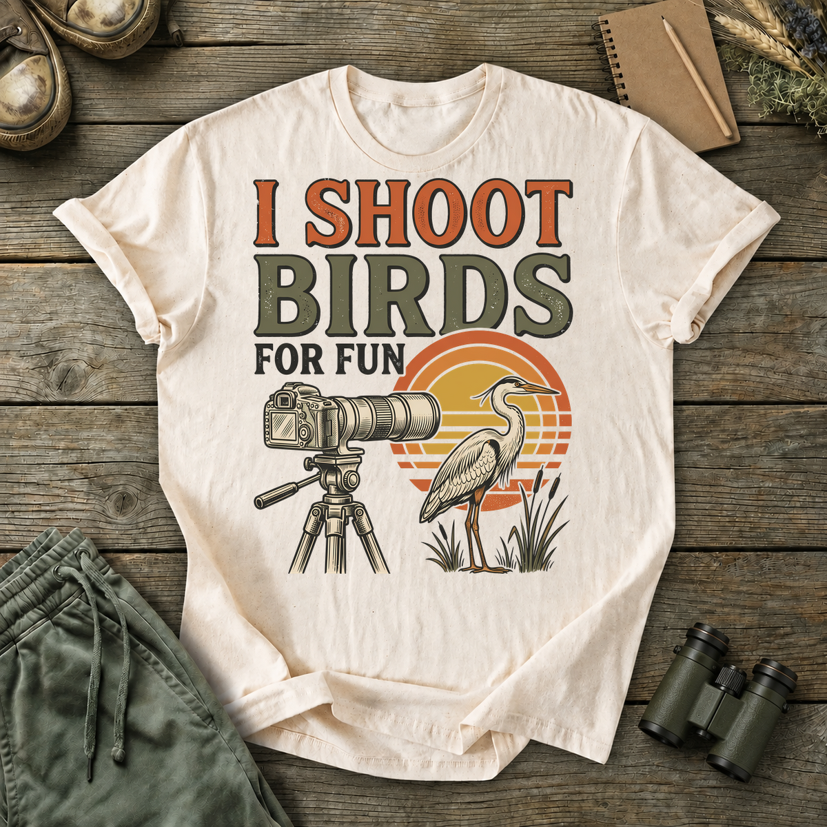 I Shoot Birds for Fun Photography Tee in Ivory, centered front design on a birdwatching flat-lay mockup