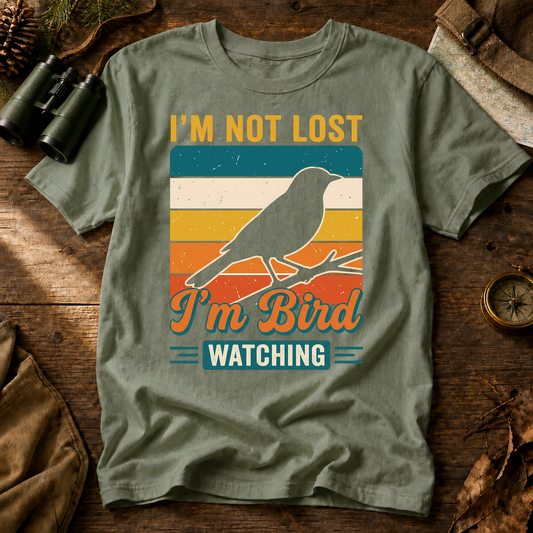 I'm Not Lost I'm Bird Watching Tee in Bay, centered front design on a birdwatching flat-lay mockup