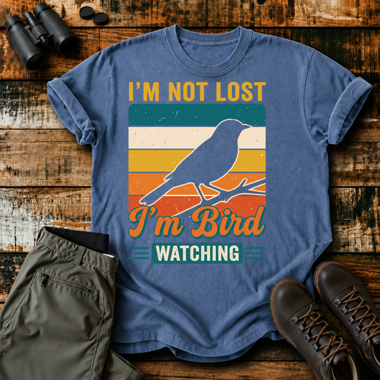 I'm Not Lost I'm Bird Watching Tee in Blue Jean, centered front design on a birdwatching flat-lay mockup