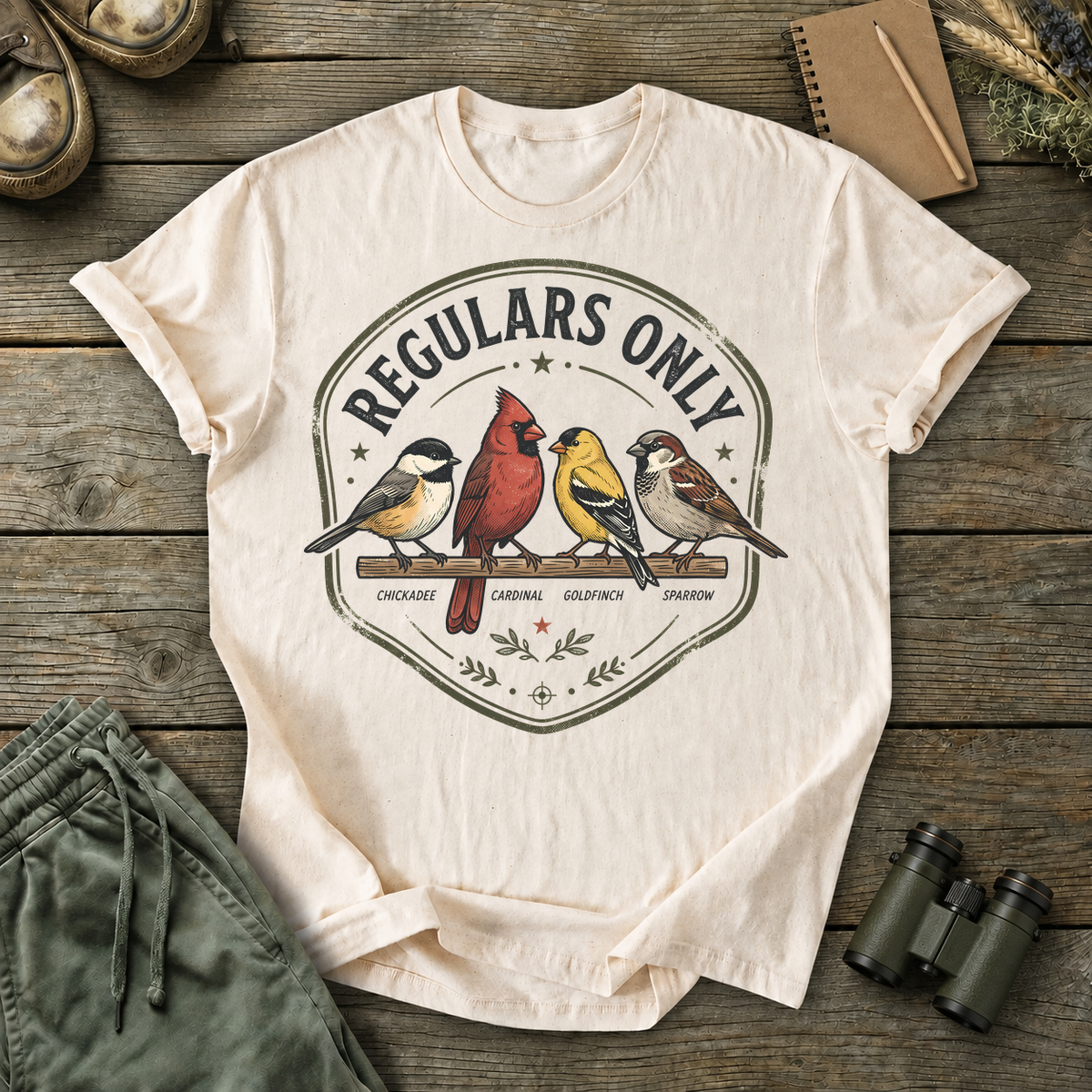 Regulars Only Backyard Birds Tee in Ivory, centered front design on a birdwatching flat-lay mockup