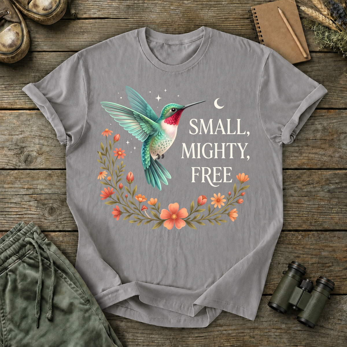 Small Mighty Free Hummingbird Tee in Grey, centered front design on a birdwatching flat-lay mockup
