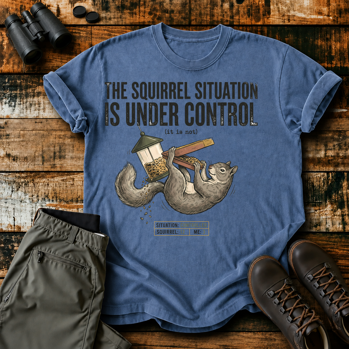 Squirrel Situation Under Control Tee in Blue Jean, centered front design on a birdwatching flat-lay mockup