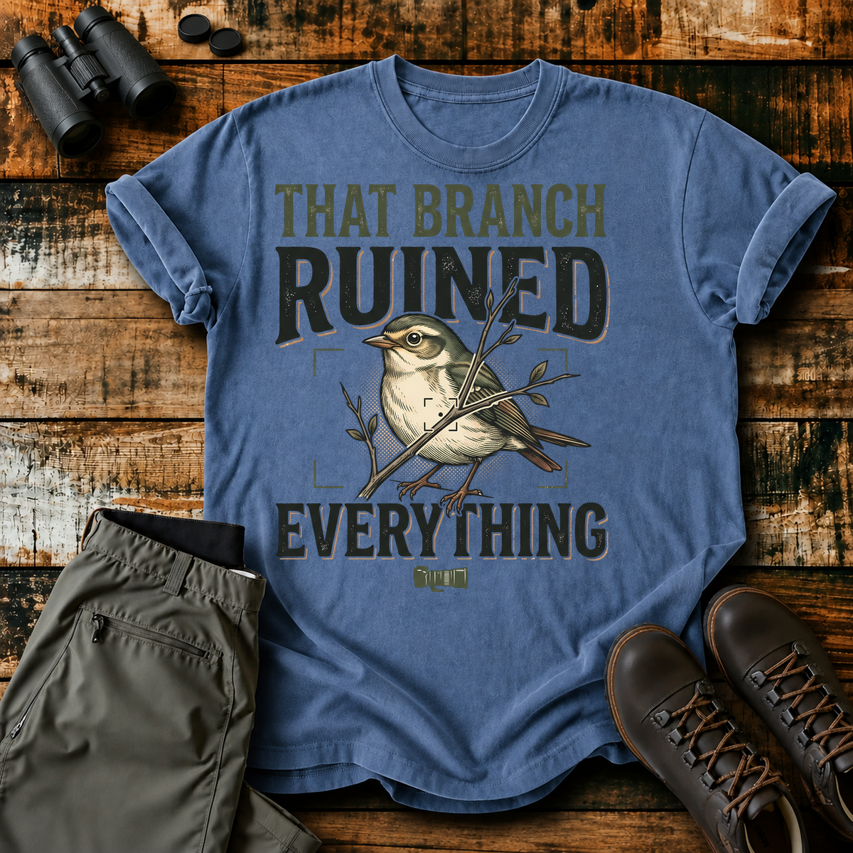 That Branch Ruined Everything Bird Photography Tee in Blue Jean, centered front design on a birdwatching flat-lay mockup