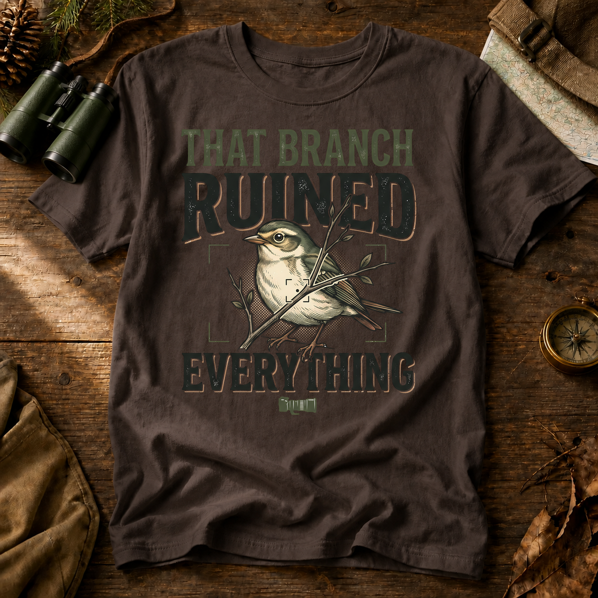 That Branch Ruined Everything Bird Photography Tee in Espresso, centered front design on a birdwatching flat-lay mockup