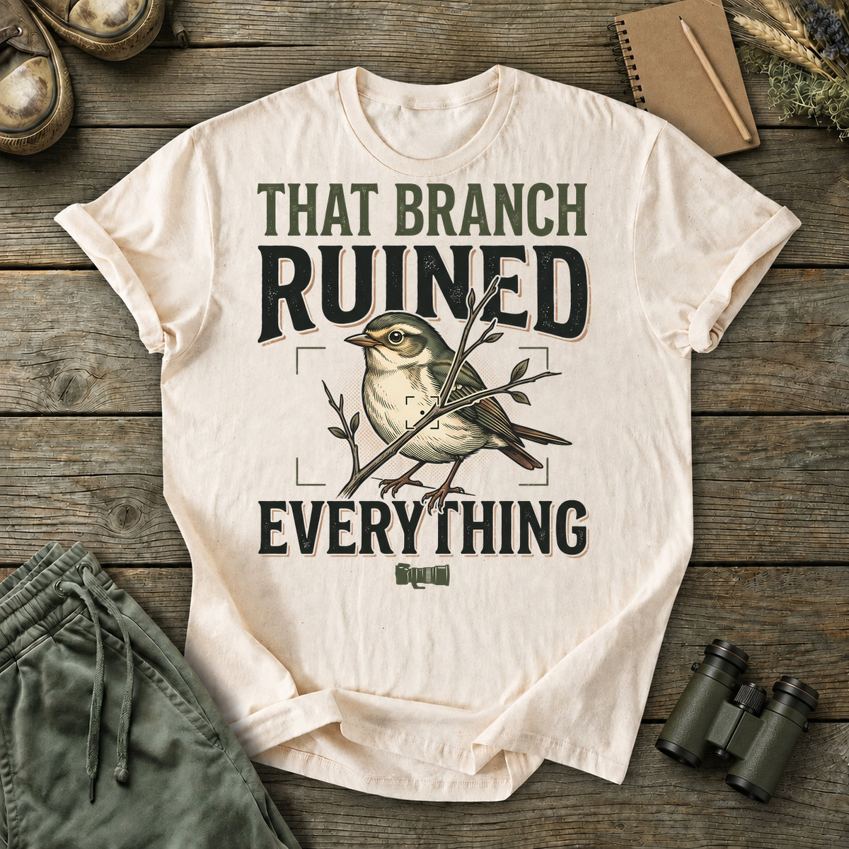 That Branch Ruined Everything Bird Photography Tee in Ivory, centered front design on a birdwatching flat-lay mockup