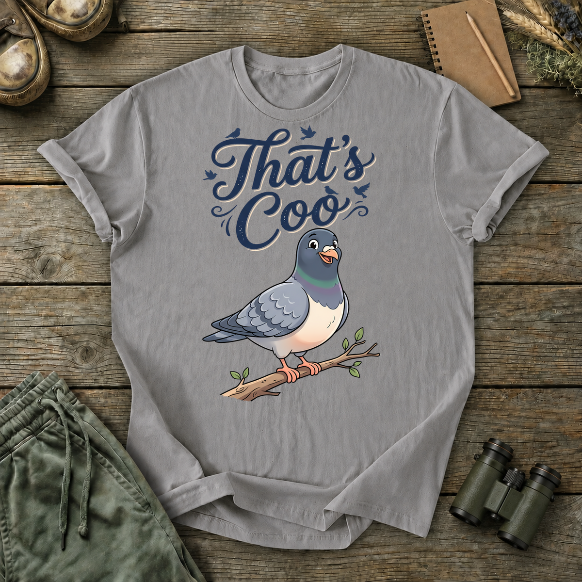 That's Coo Pigeon Tee in Grey, centered front design on a birdwatching flat-lay mockup