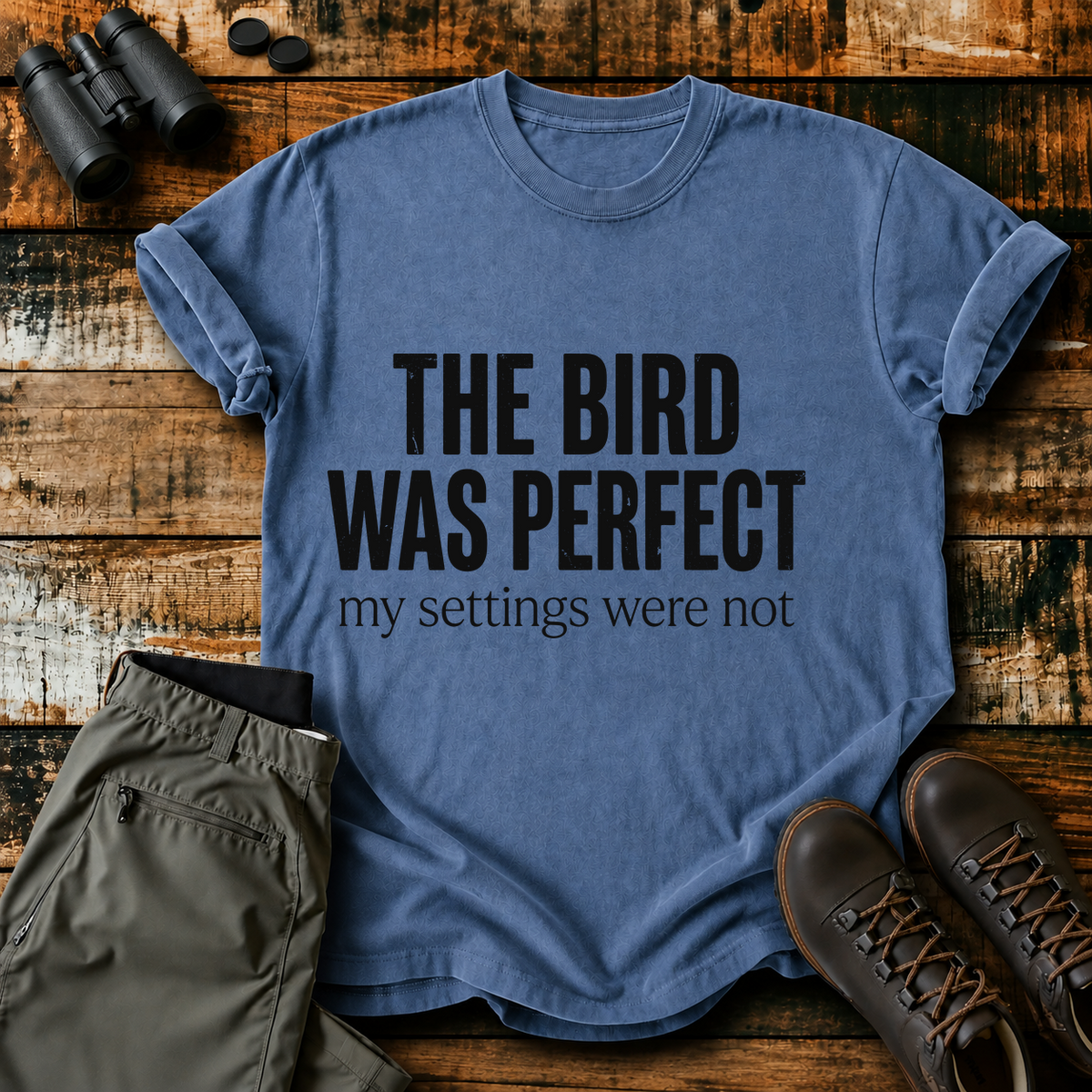 The Bird Was Perfect My Settings Were Not Tee in Blue Jean, centered front design on a birdwatching flat-lay mockup