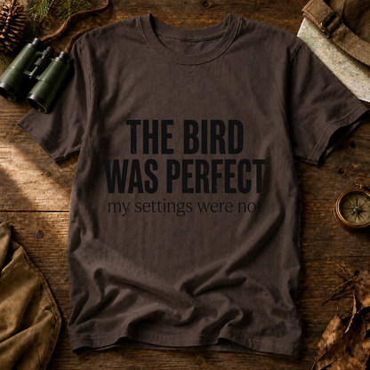 The Bird Was Perfect My Settings Were Not Tee in Espresso, centered front design on a birdwatching flat-lay mockup