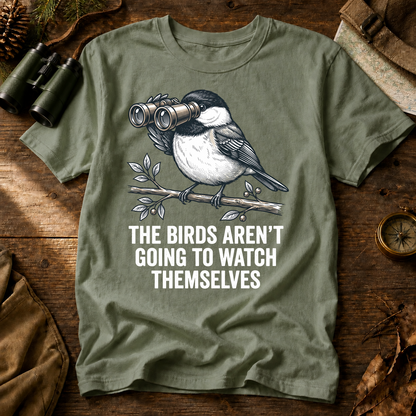 The Birds Aren't Going to Watch Themselves Tee in Bay, centered front design on a birdwatching flat-lay mockup
