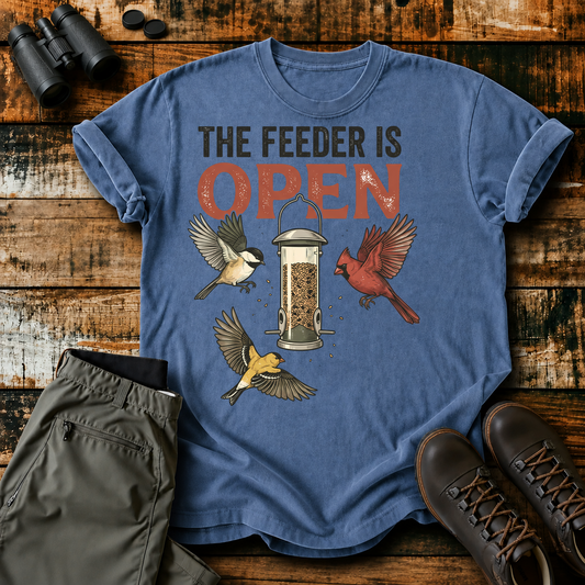 The Feeder Is Open Backyard Birds Tee in Blue Jean, centered front design on a birdwatching flat-lay mockup