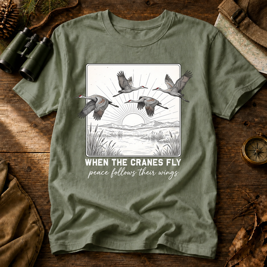 When the Cranes Fly Peace Follows Tee in Bay, centered front design on a birdwatching flat-lay mockup