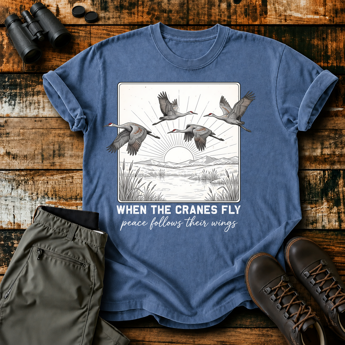 When the Cranes Fly Peace Follows Tee in Blue Jean, centered front design on a birdwatching flat-lay mockup