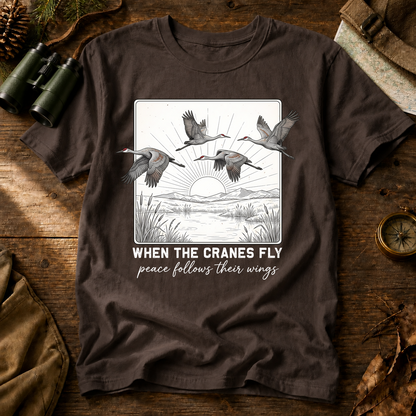 When the Cranes Fly Peace Follows Tee in Espresso, centered front design on a birdwatching flat-lay mockup