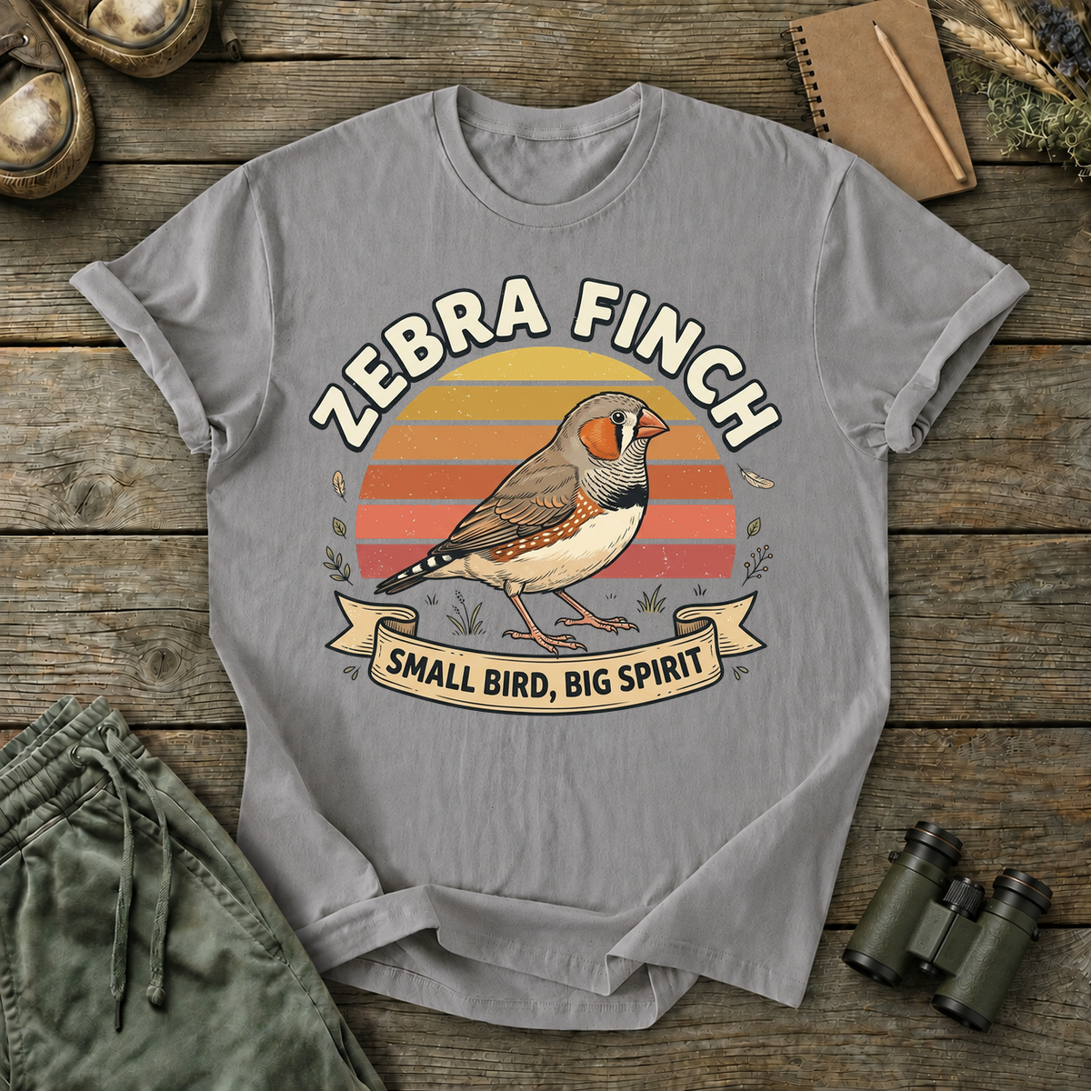 Zebra Finch Small Bird Big Spirit Tee in Grey, centered front design on a birdwatching flat-lay mockup
