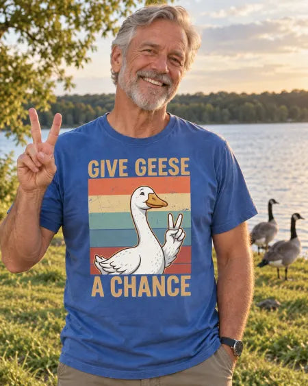 AI-created lifestyle scene: a smiling man wearing the Blue Jean Give Geese a Chance tee beside a lake with geese.